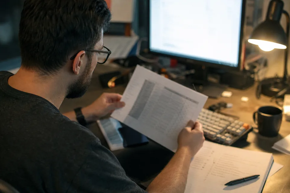 Marketer checking a printed DNS sheet against a monitor