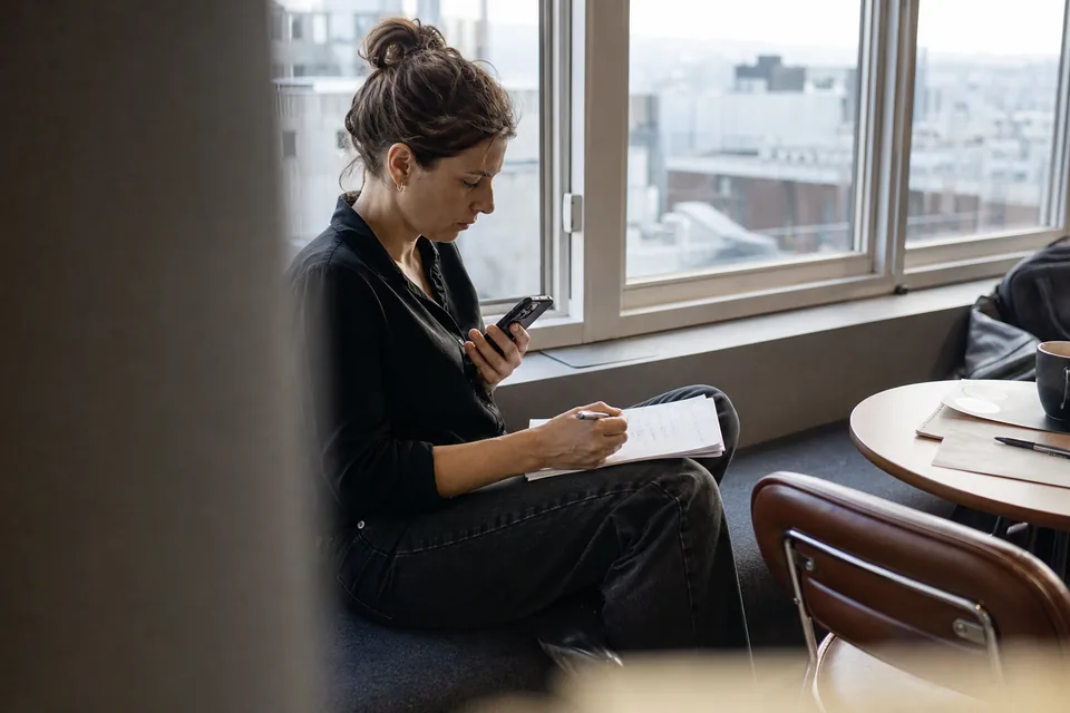 Account executive crossing off a paper task list while holding a phone