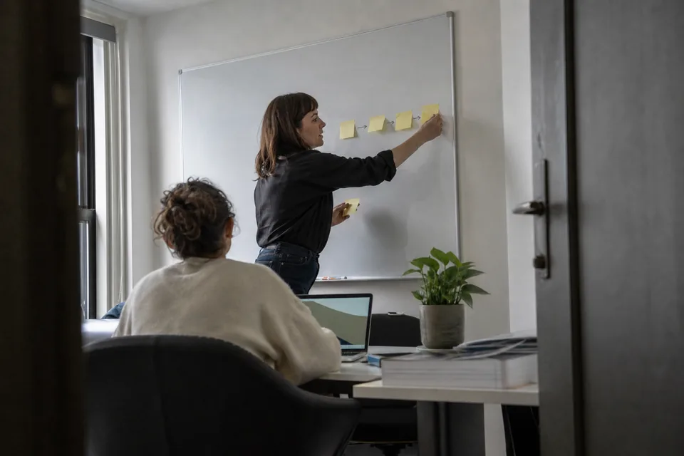 Agency team lead placing sticky notes in a row on a whiteboard to map an outreach sequence